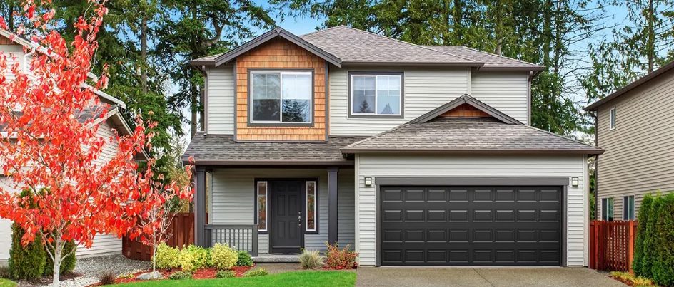 Two‑story house with dark raised‑panel double garage door and red autumn tree in front yard