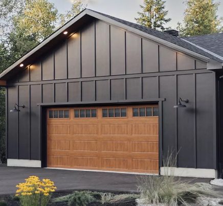 Black board‑and‑batten garage with warm wood‑look door and small top windows at dusk